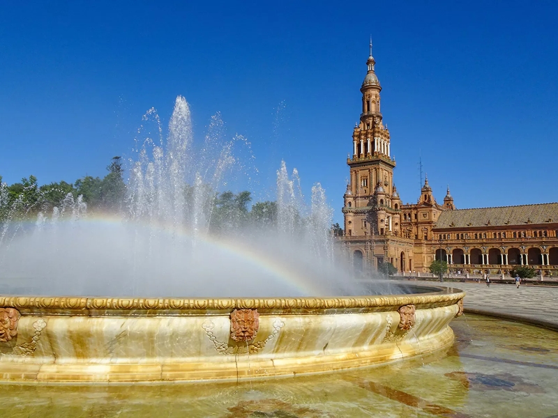 Fontein met regenboog voor historische toren in Sevilla