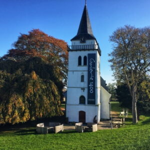 Historische kerktoren met galerie, omgeven door herfstbomen.