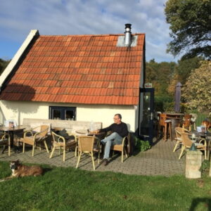 Kleine huis met terras en zittende man.
