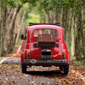 Rode retro auto rijdt op bosweg in de herfst.