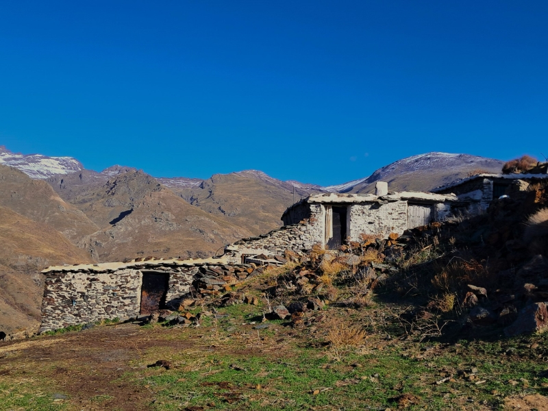 Stenen huisje in berglandschap met blauwe lucht.