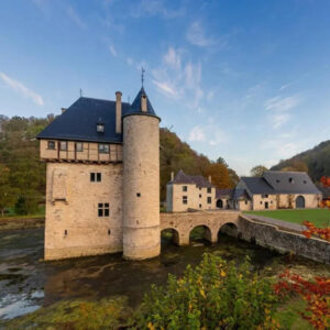 Middeleeuws kasteel met toren en brug in herfstlandschap.