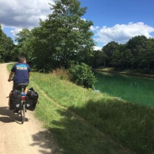 Fietser op zandweg langs kanaal en bomen.