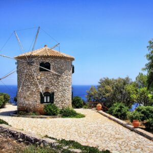 Stenen windmolen aan zee onder blauwe lucht.