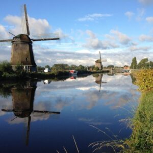 Windmolens weerspiegeld in het water onder blauwe lucht.
