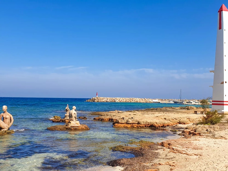 Kust met beelden en vuurtoren bij blauwe zee