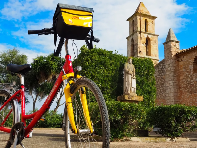 Fiets bij kerk en standbeeld op zonnige dag