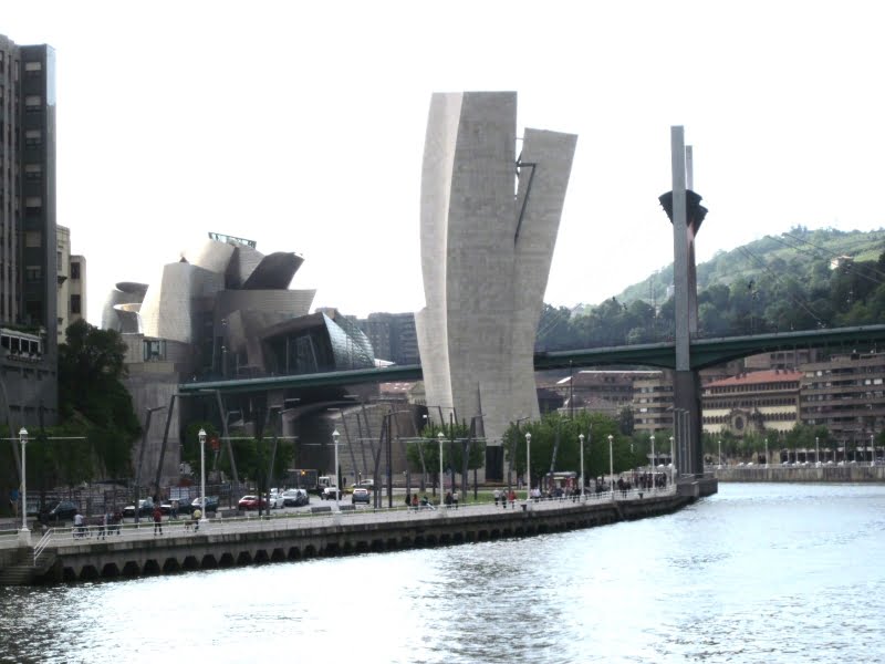 Modern gebouw aan de rivier met brug op achtergrond.