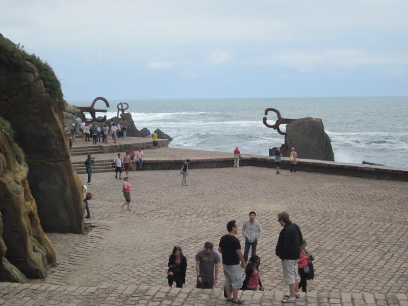 Mensen bij de kust met beeldhouwwerken langs de zee.
