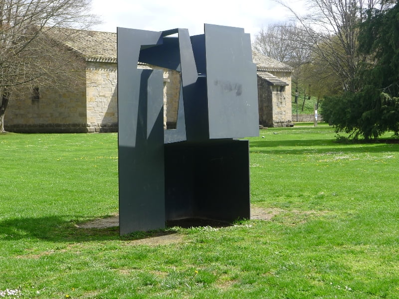 Abstract beeldhouwwerk op grasveld bij stenen gebouw.
