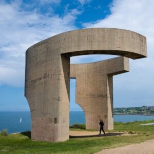 Monument aan zee met wandelaar eronder.