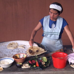 Vrouw maakt tortilla's op traditioneel kookoppervlak.