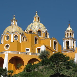 Geelgeschilderde kerk op groene heuvel, blauwe lucht.
