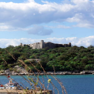 Oud fort op heuvel met zee op voorgrond.