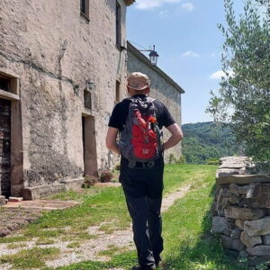 Wandelaar met rugzak naast oud gebouw op zonnige dag.
