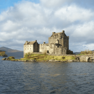 Middeleeuws kasteel aan meer met brug en heuvels.