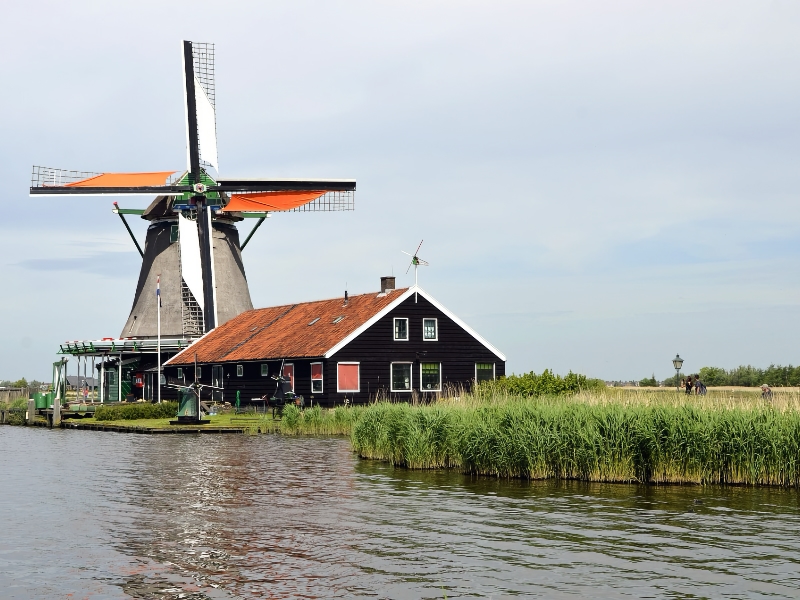 Nederlandse molen naast traditioneel huis aan waterkant.