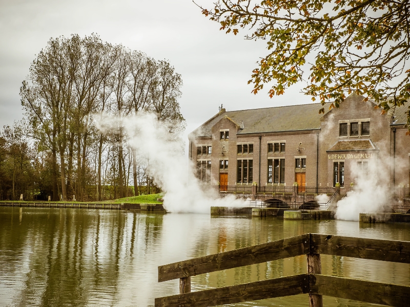 Historisch gemaal aan rustige rivier met stoomwolken.