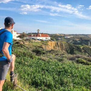 Wandelaar op heuvel, uitzicht op huizen en kust.
