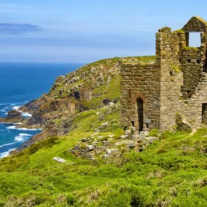 Oude stenen ruïne aan zee met groene heuvels.
