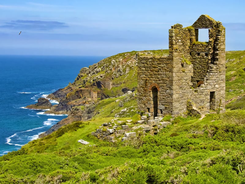 Oude stenen ruïne aan zee met groene heuvels.