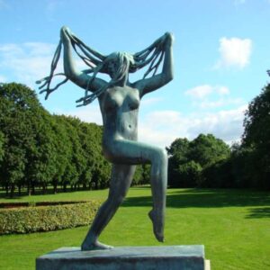 Dansende bronzen vrouwensculptuur in park met blauwe lucht.