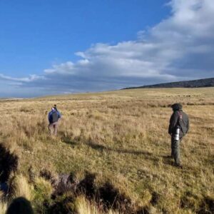 Twee wandelaars in een open veld met blauwe lucht.