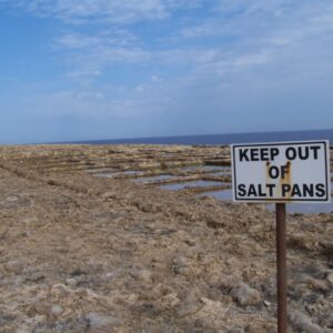 Waarschuwingsbord bij zoutpannen, zee op achtergrond.