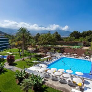 Luxe hotel zwembad met tuin en bergen op achtergrond.