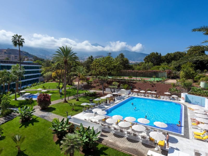 Luxe hotel zwembad met tuin en bergen op achtergrond.