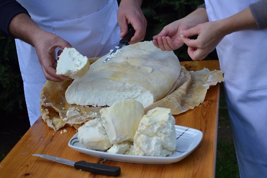 Personen snijden grote kaas op houten tafel.