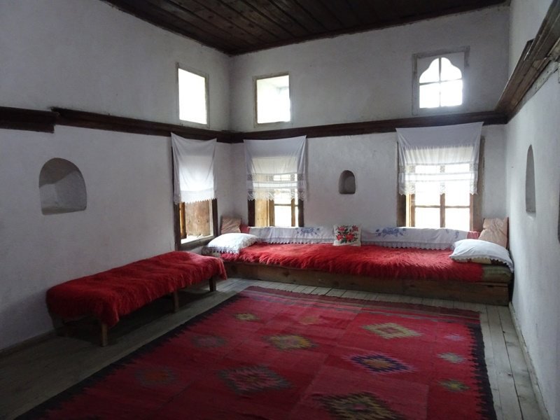 Traditionele kamer met rode tapijten en houten zitbanken.