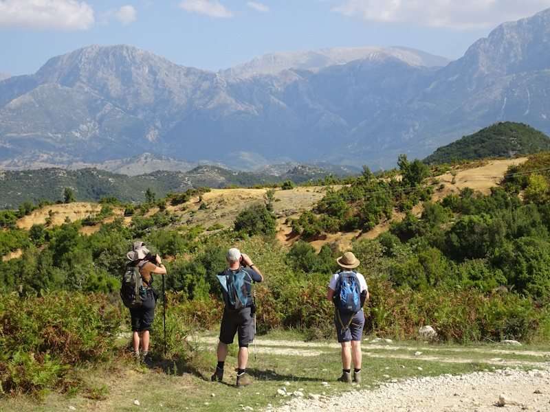 Wandelaars in groene bergen met blauwe lucht.