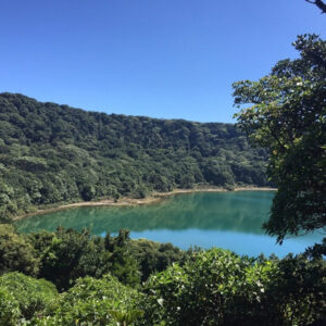 Blauw meer omgeven door groene bomen en heuvels.