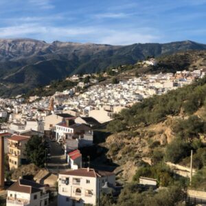 Wit dorp op heuvels bij bergen onder blauwe lucht.