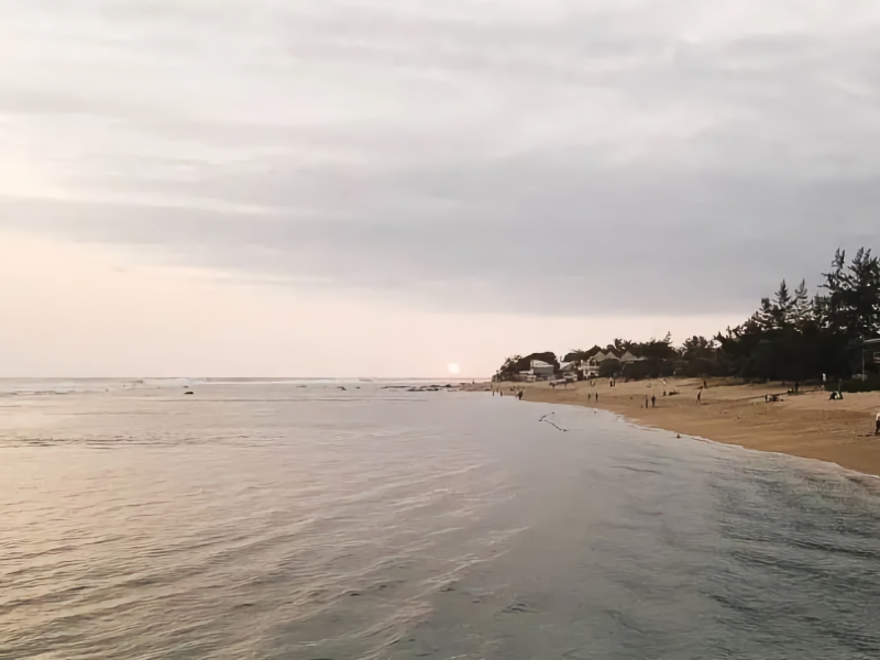 Strand bij zonsondergang met kalme zee en huizen.