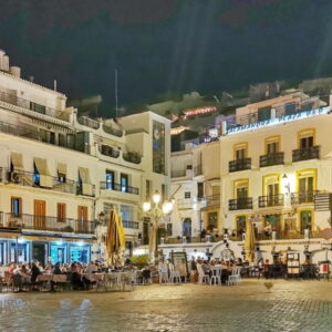 Avondstadscène met druk bezocht plein en gebouwen.
