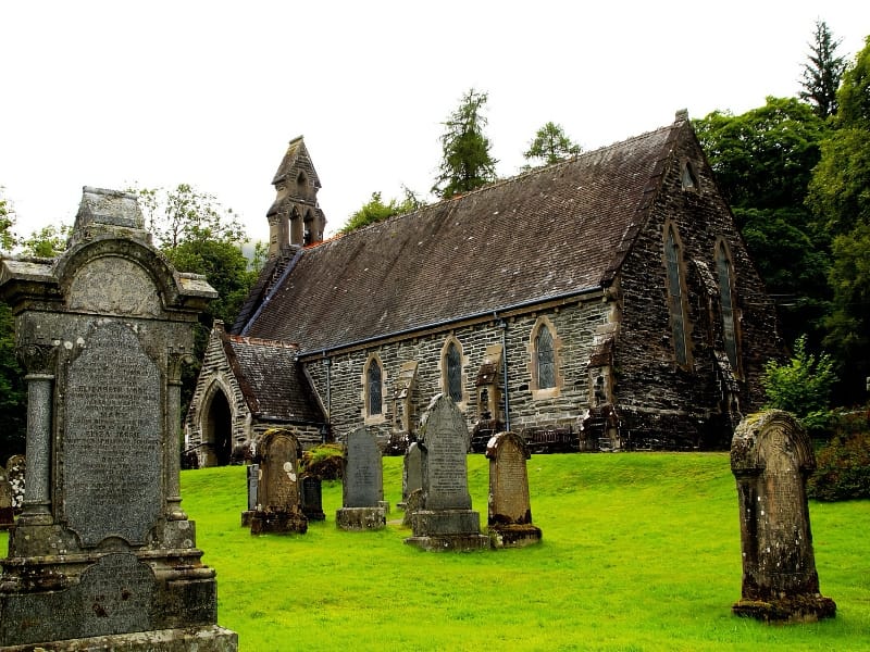 Oude stenen kerk met kerkhof op groene heuvel.
