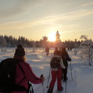Groep wandelt op sneeuwschoenen bij zonsopgang in bos.